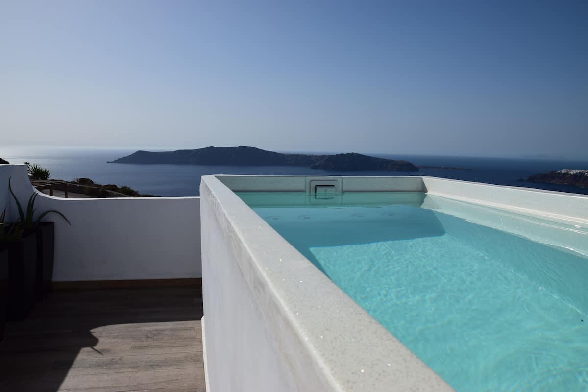 A rooftop infinity pool with clear blue water, overlooking a coastal landscape with distant islands.