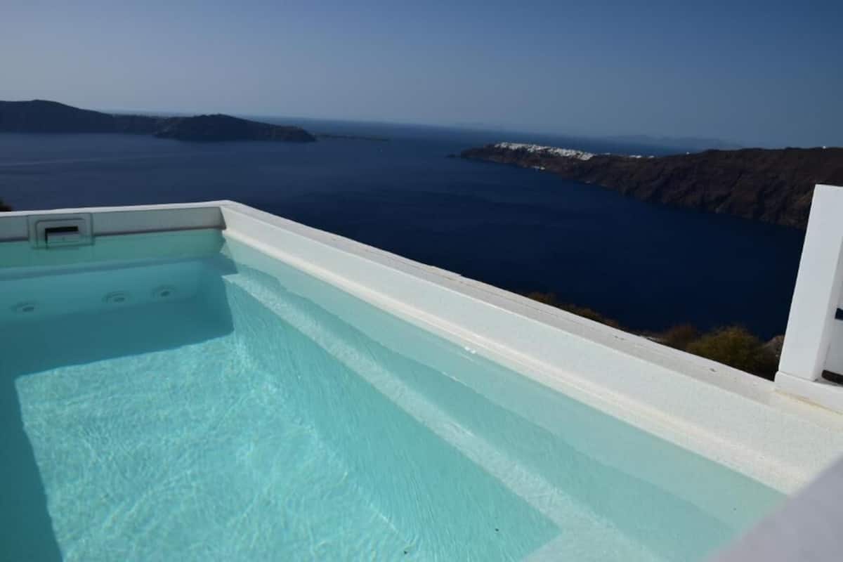 A clear view of a swimming pool with a white edge, overlooking a coastal landscape with cliffs and the sea.