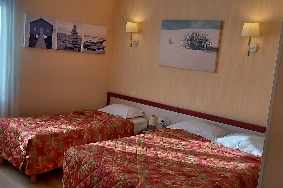 Habitación de hotel con dos camas, cada una con cubrecama floral, cabecera de madera y lámparas fijadas a la pared. Se observan cuadros enmarcados en la pared.
