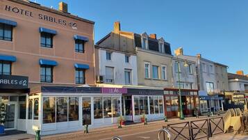 Une rangée de bâtiments, avec un hôtel appelé HOTEL SABLES D'O sur la gauche, un restaurant appelé LE 16 BIS au centre, et d'autres boutiques en arrière-plan.