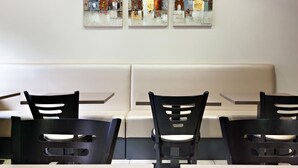 Un comedor con asientos tipo cabina, tres cuadros en la pared y modernas sillas negras con diseños recortados.