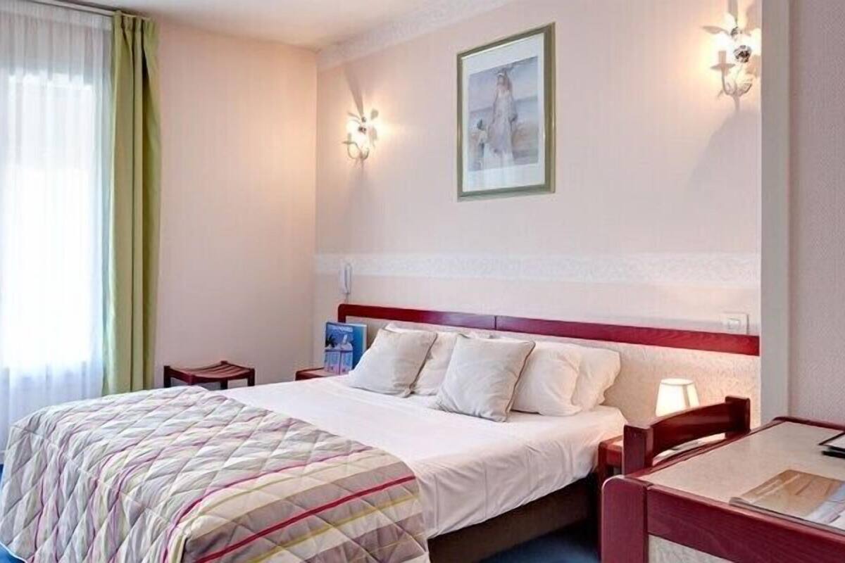 Una habitación de hotel con cama, mesita de noche, una mesa y una ventana con cortinas.
