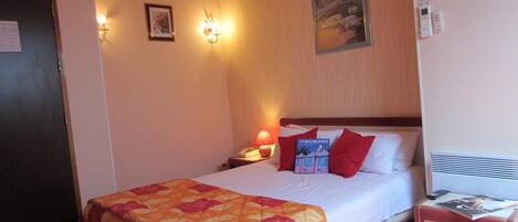 A hotel room with a bed, a nightstand, a lamp, a framed picture, and a wall-mounted light fixture.