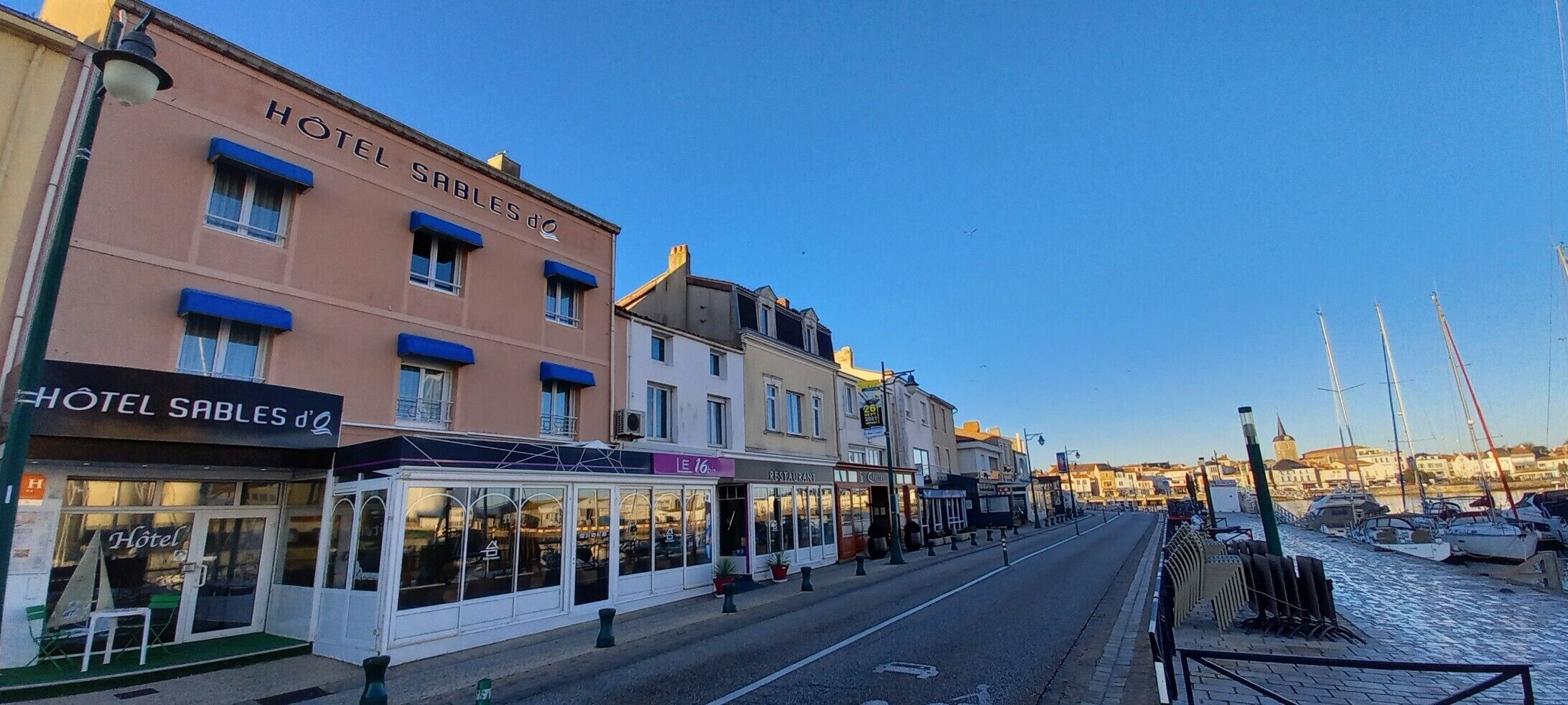A street view of Hotel Sables d'O, featuring a row of buildings with a restaurant and a café on the ground floor.