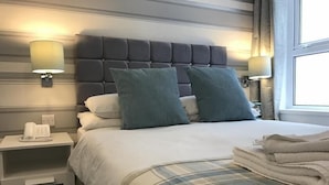 Un lit bien fait, recouvert d’une couverture à carreaux, avec deux oreillers assortis et une table de chevet sur laquelle se trouvent une lampe et un téléphone.