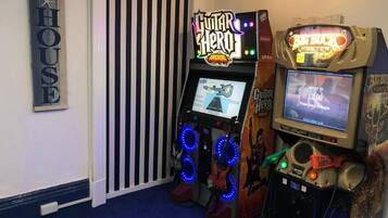 A room with a striped wall, a neon sign for 'Guitar Hero', and a 'Big Buck Hunter' game machine.