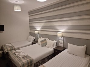 A hotel room with two single beds, each with a nightstand and a lamp. The room has a striped wall design and a ceiling light. - Tiffanys Hotel (Blackpool)