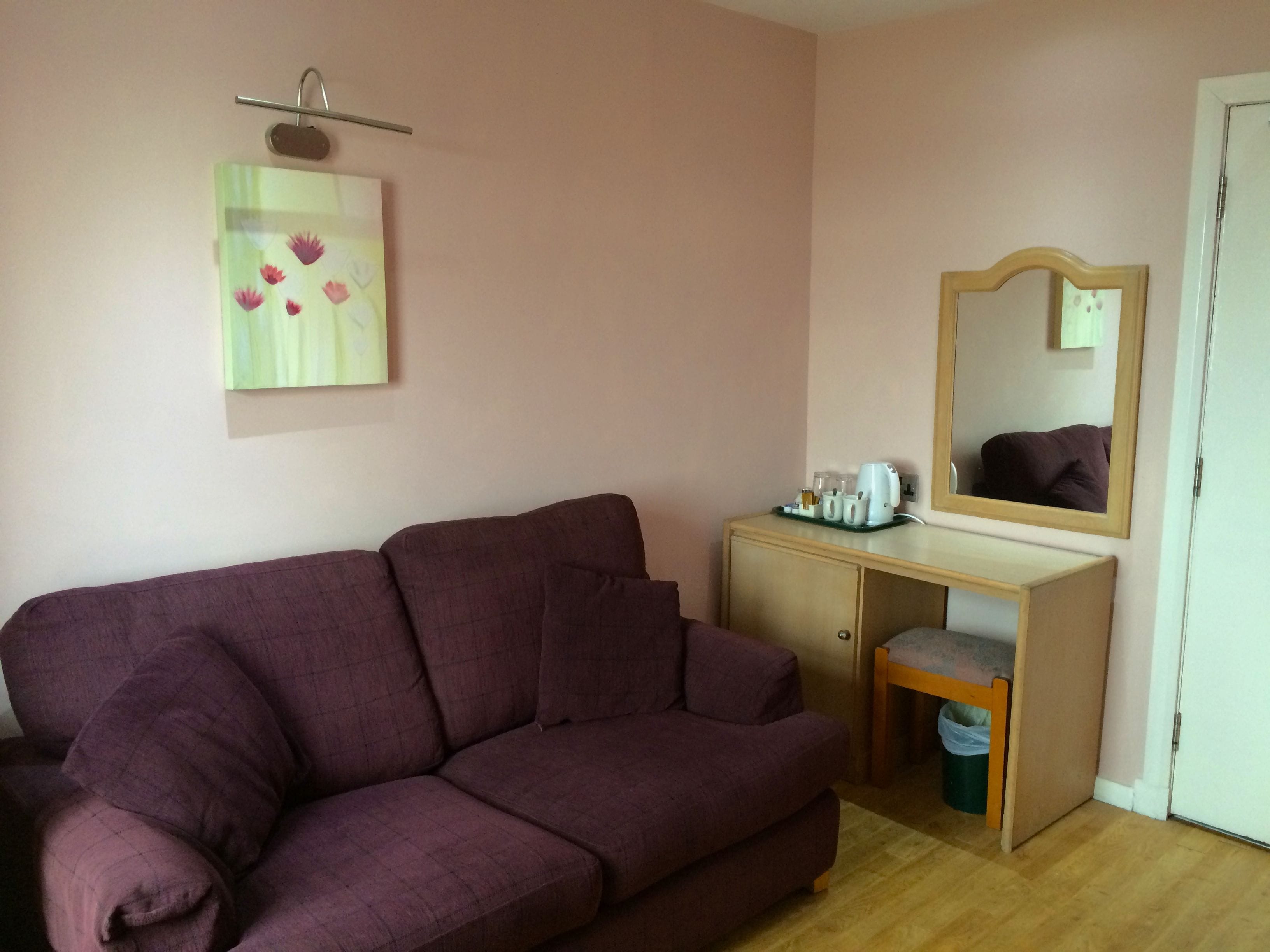 A room with a purple sofa, a wooden desk with a mirror, and a small trash bin.