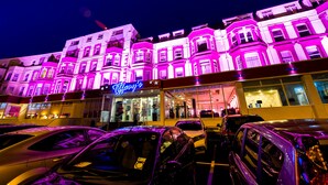 Un hôtel avec une enseigne au néon, de nombreux étages et des voitures garées devant.