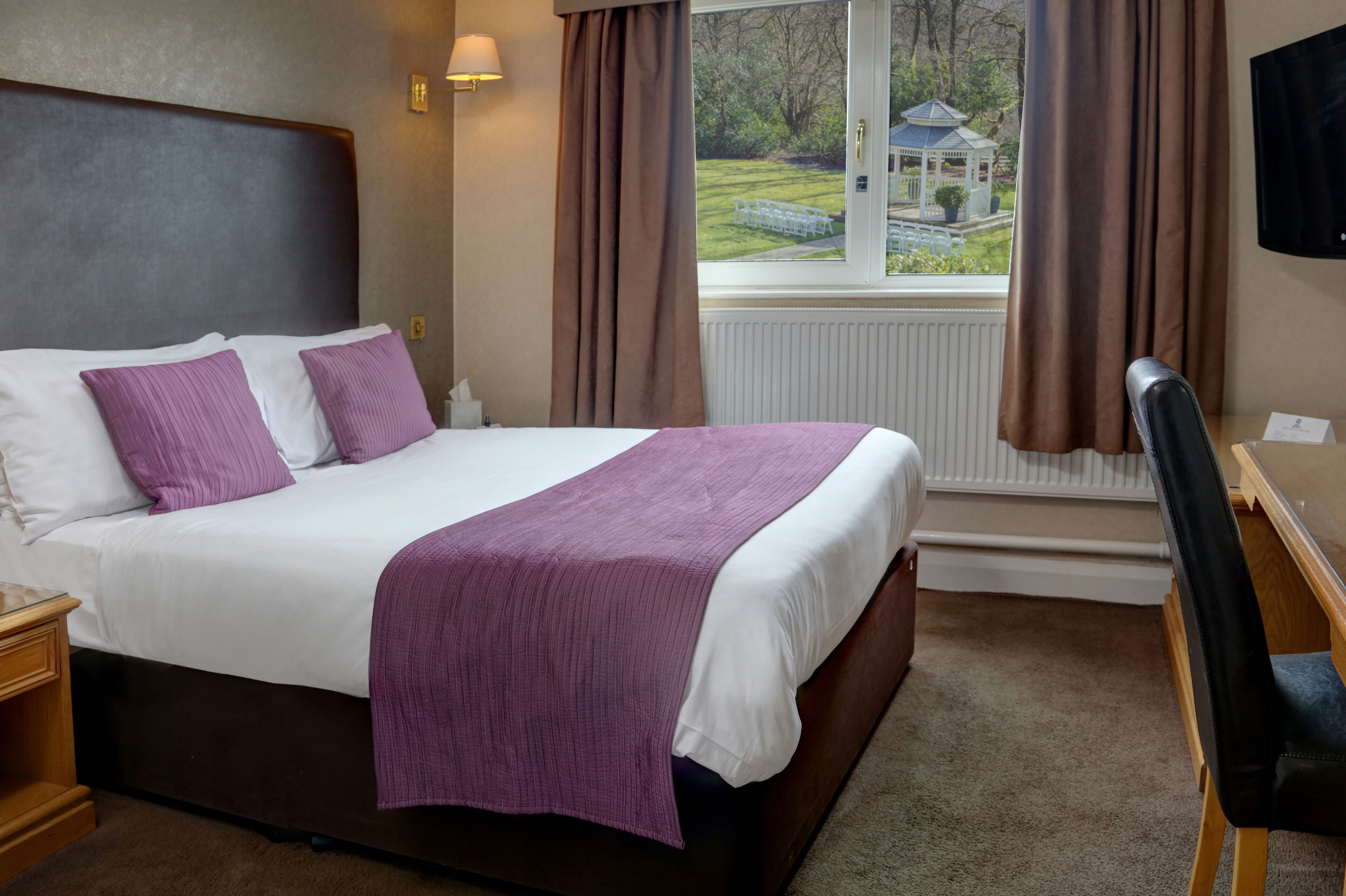 A hotel room with a large bed, a desk, a chair, and a window with curtains.