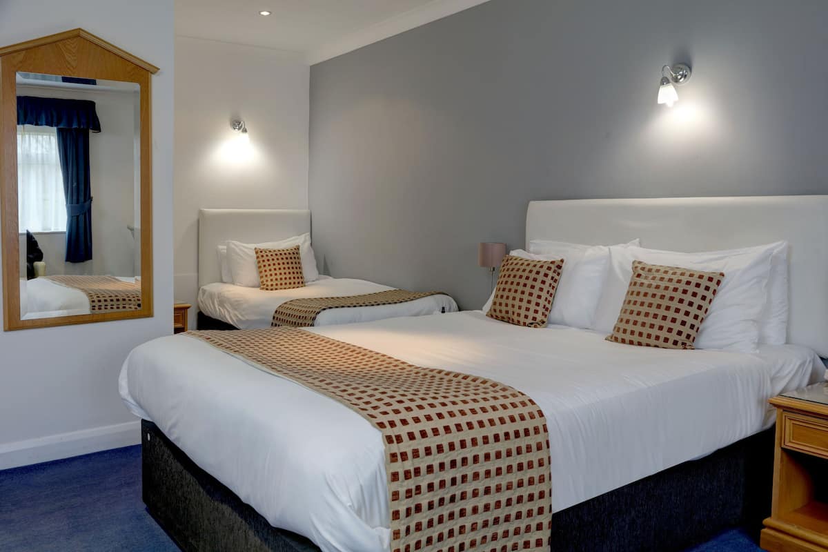 A hotel room with a large bed, a bedside table, a mirror, and a wall-mounted light fixture.
