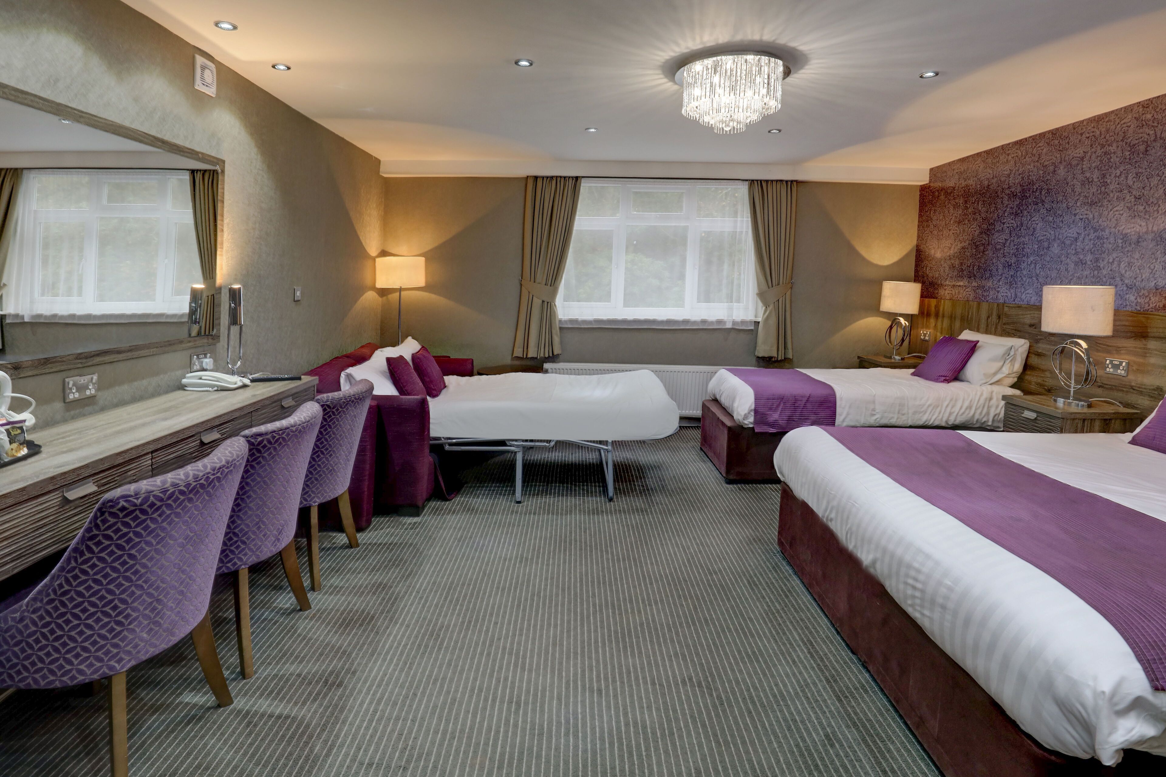 A hotel room with two beds, a desk, chairs, and a chandelier.