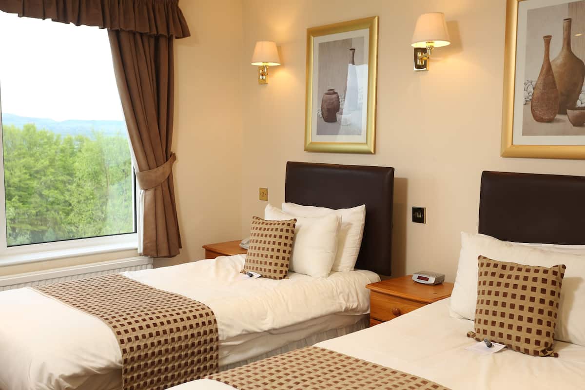 A hotel room with two beds, a large window with curtains, wall-mounted lamps, and framed artwork.