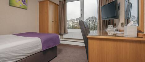Habitación de hotel con cama, escritorio, computadora, televisor y ventana con cortinas.