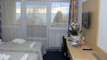 Habitación de hotel con dos camas, un escritorio, una silla, un televisor y un ventanal con cortinas.