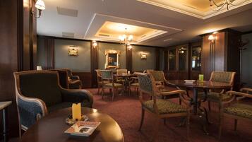 A hotel room with a round dining table, several upholstered chairs, a chandelier, and a mirror on the wall.