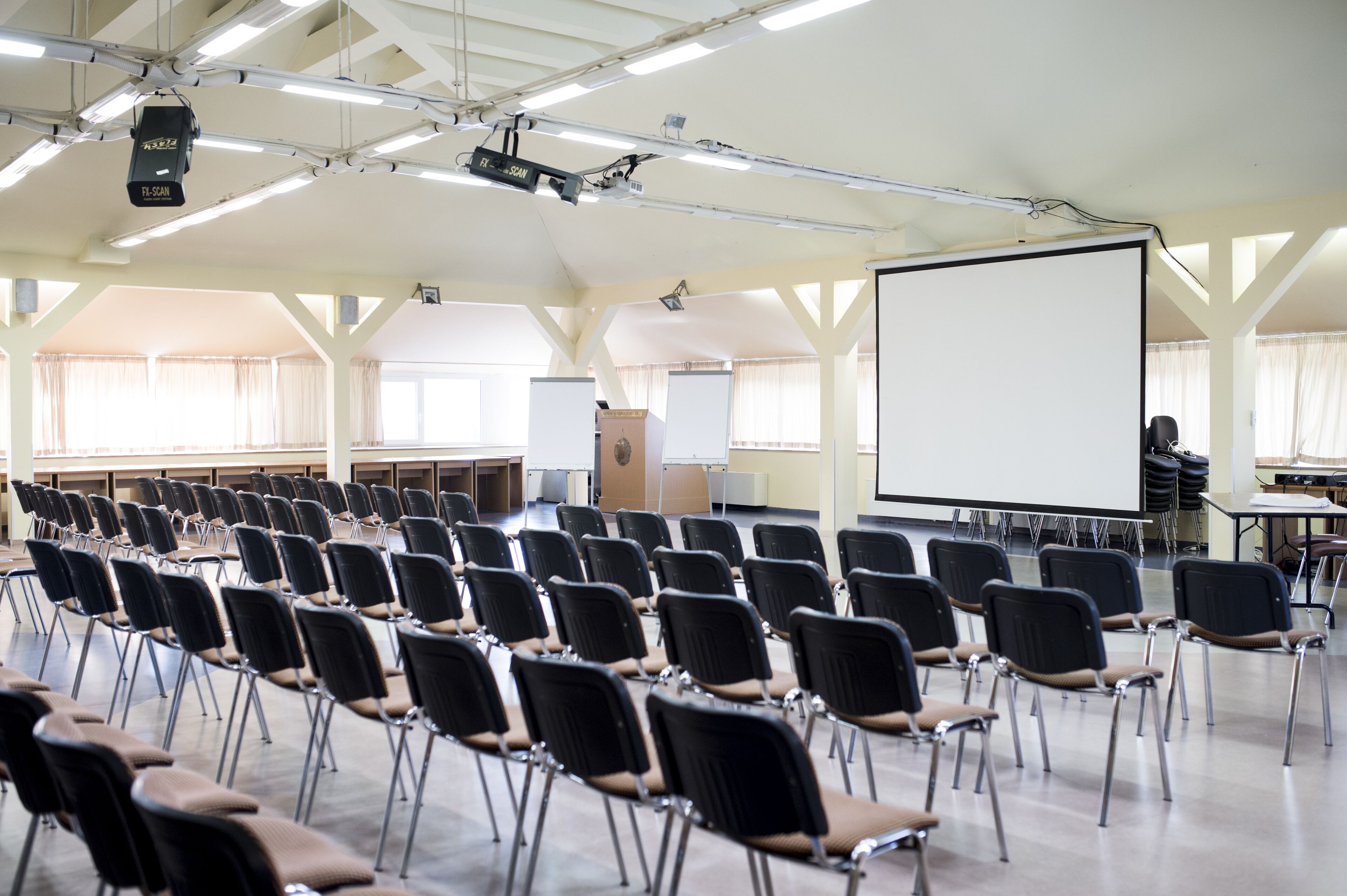 Une salle de conférence avec des rangées de chaises, un grand écran et un projecteur.
