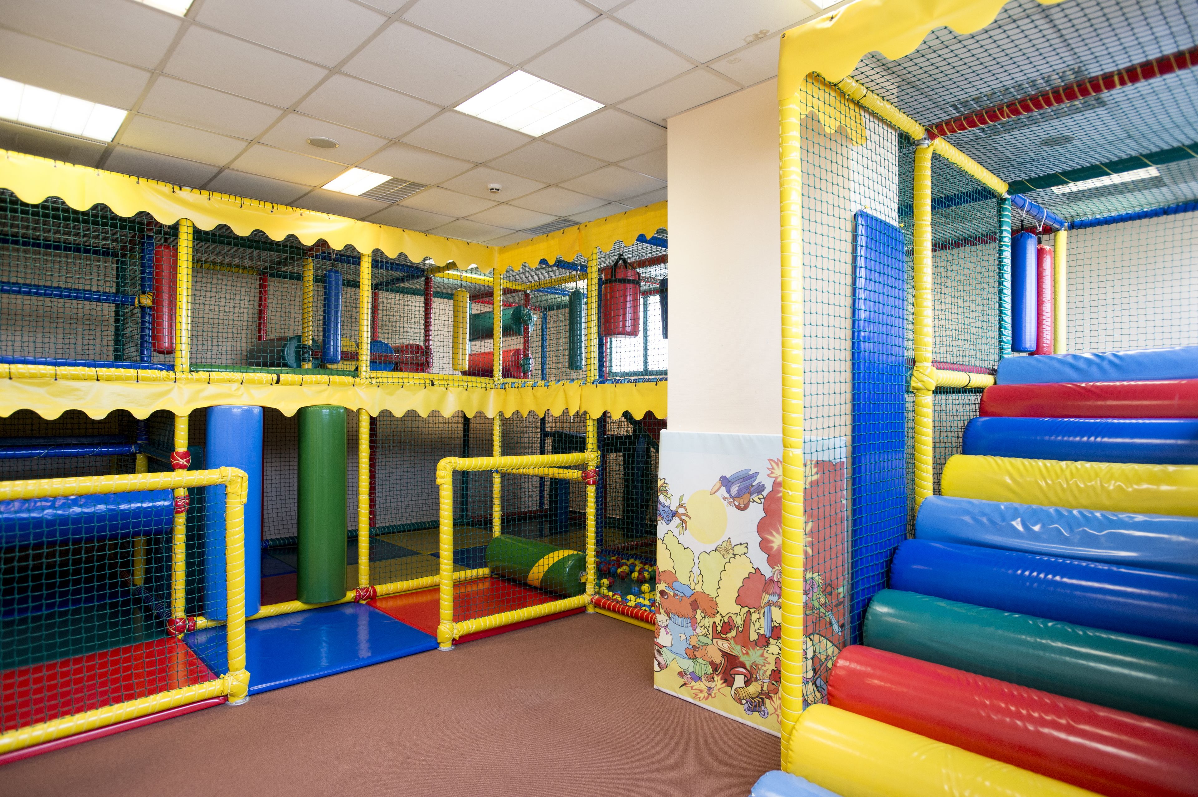A multi-level indoor play area with netted walls and padded flooring.