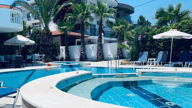 A swimming pool with lounge chairs and umbrellas, surrounded by palm trees and a building labeled "White Palace". - White Palace Studios (Rhodes)