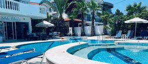 A swimming pool with lounge chairs and umbrellas, surrounded by palm trees and a building labeled "White Palace". - White Palace Studios (Rhodes)