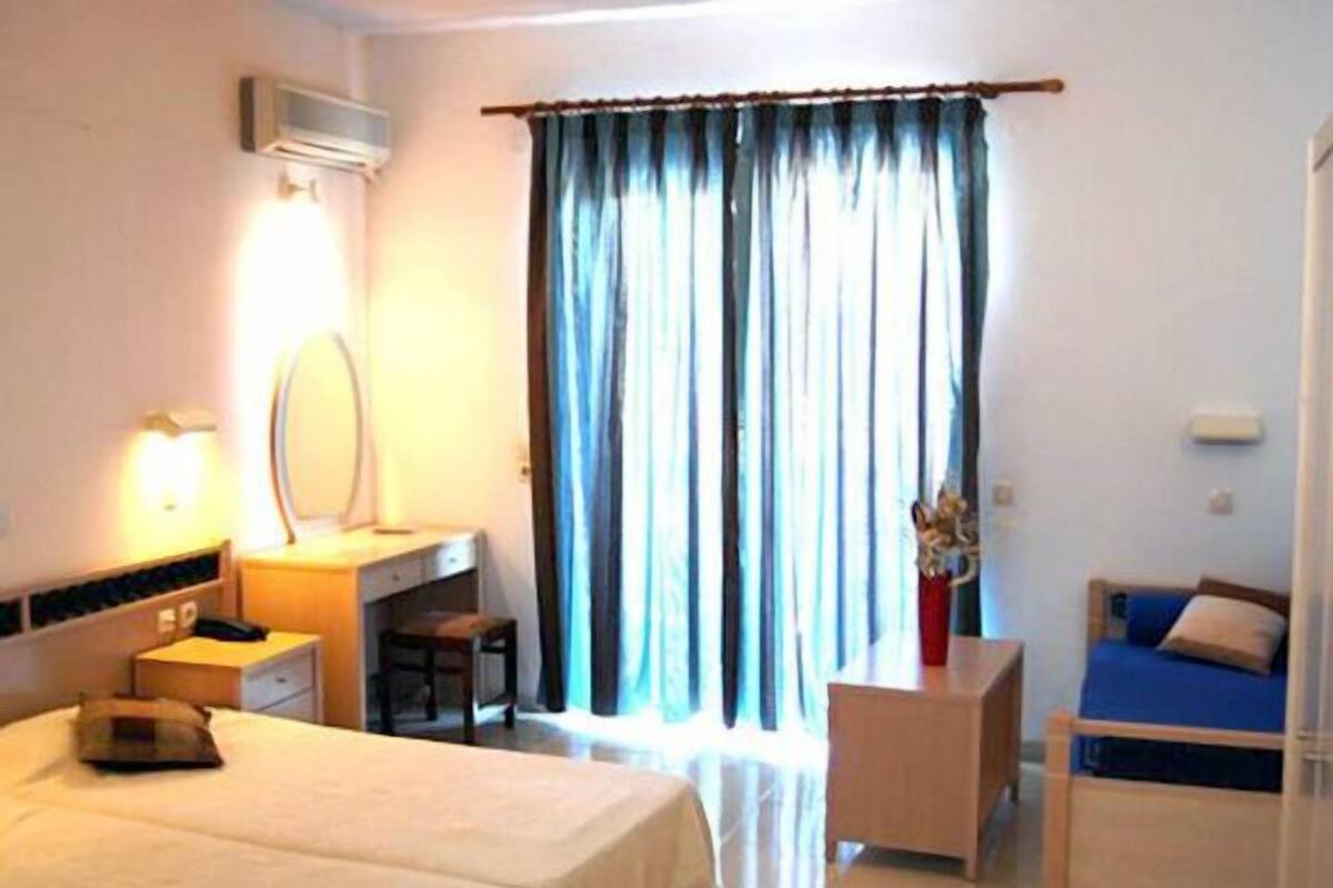A hotel room with two beds, a desk, a chair, and a window with curtains.