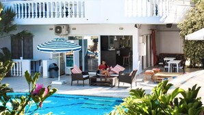 A poolside area with lounge chairs, a striped umbrella, and a view of the pool. - White Palace Studios (Rhodes)