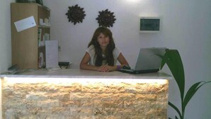 A reception desk with a stone facade, a laptop, and a potted plant. - White Palace Studios (Rhodes)