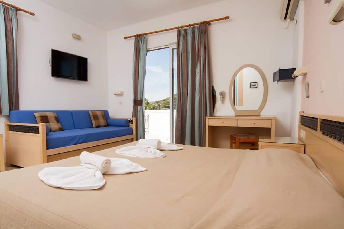 A hotel room with a bed, a blue sofa, a wooden desk, a mirror, and a TV.