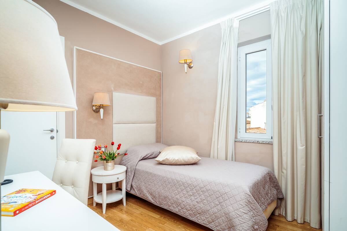 Um quarto com uma cama, uma mesa de cabeceira com abajur, uma cadeira e uma janela com cortinas.