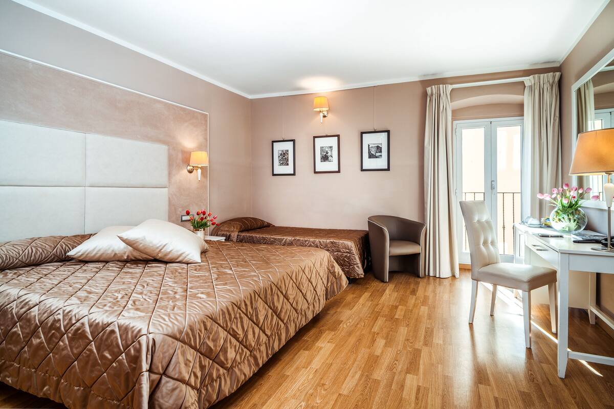 Quarto de hotel com uma cama grande, uma escrivaninha, uma cadeira e uma janela com cortinas.