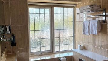 A modern bathroom with a large window, a sink, a toilet, and a bathtub.