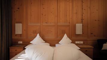 A hotel room with a wooden paneled headboard, two bedside tables, a bed with white bedding, and a chair.
