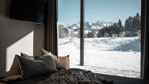Un dormitorio con cama, almohadas y manta. Un televisor está montado en la pared.