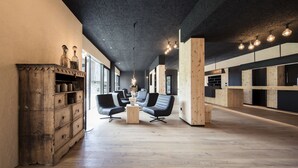 Una habitación amplia con suelo de madera, un aparador de madera antiguo y sillas de cuero negro modernas.