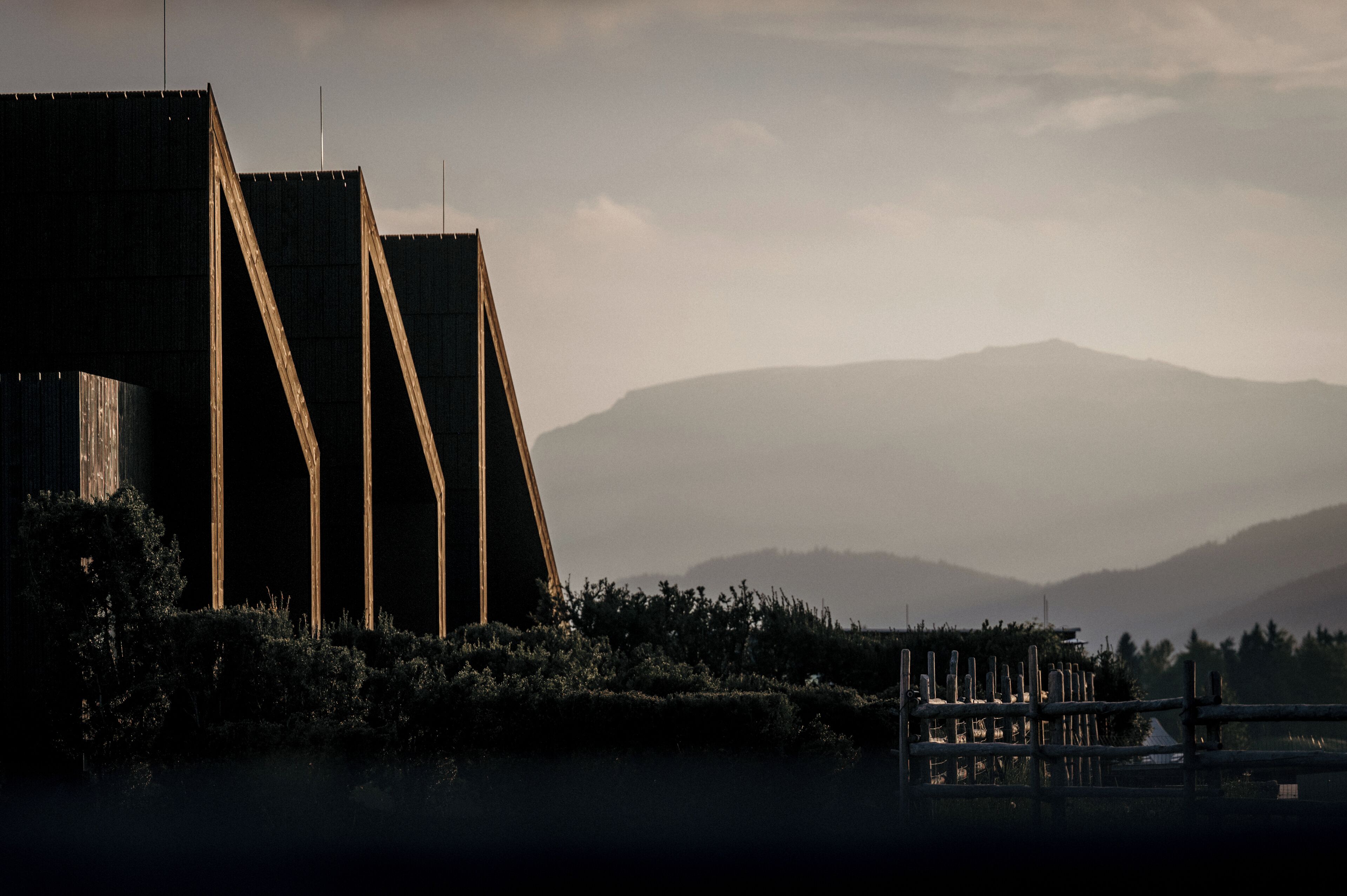 Un edificio moderno con una estructura de techo triangular única, rodeado por un paisaje natural con colinas al fondo.