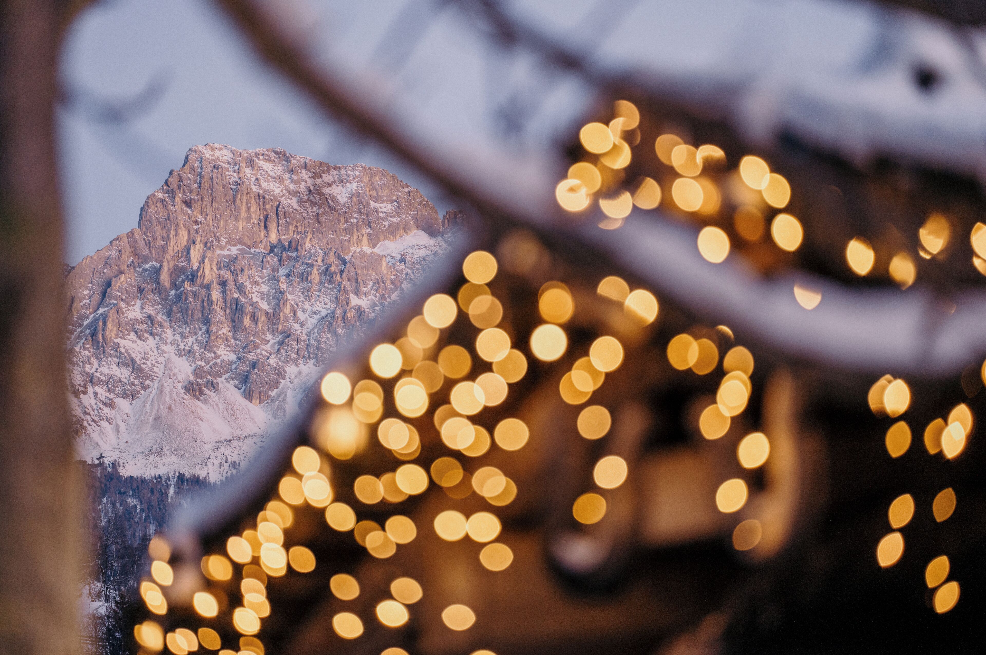 A mountain landscape with snow-covered peaks and bokeh lights in the foreground.