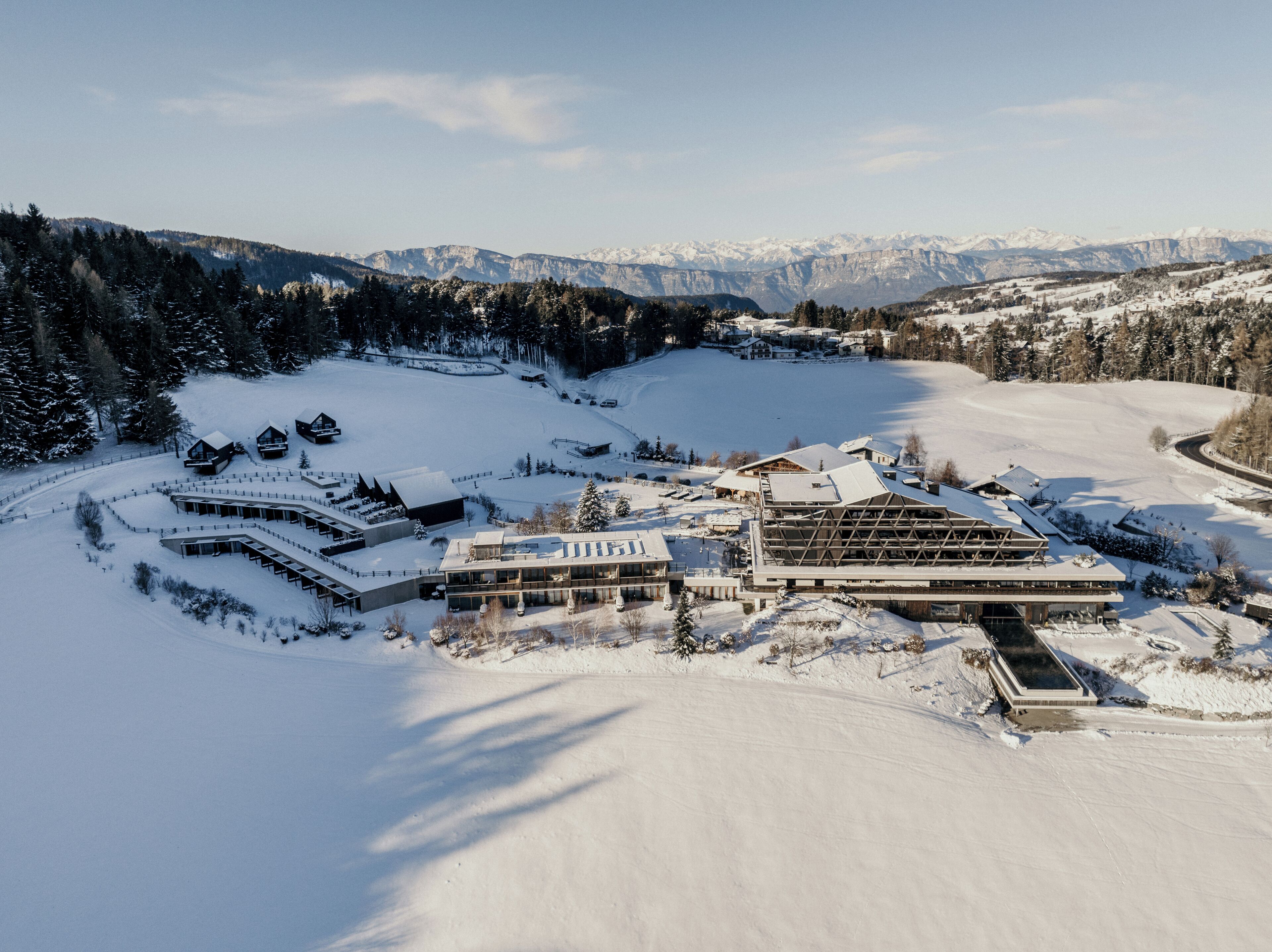 A snow-covered resort with modern buildings, a ski slope, and mountainous views.