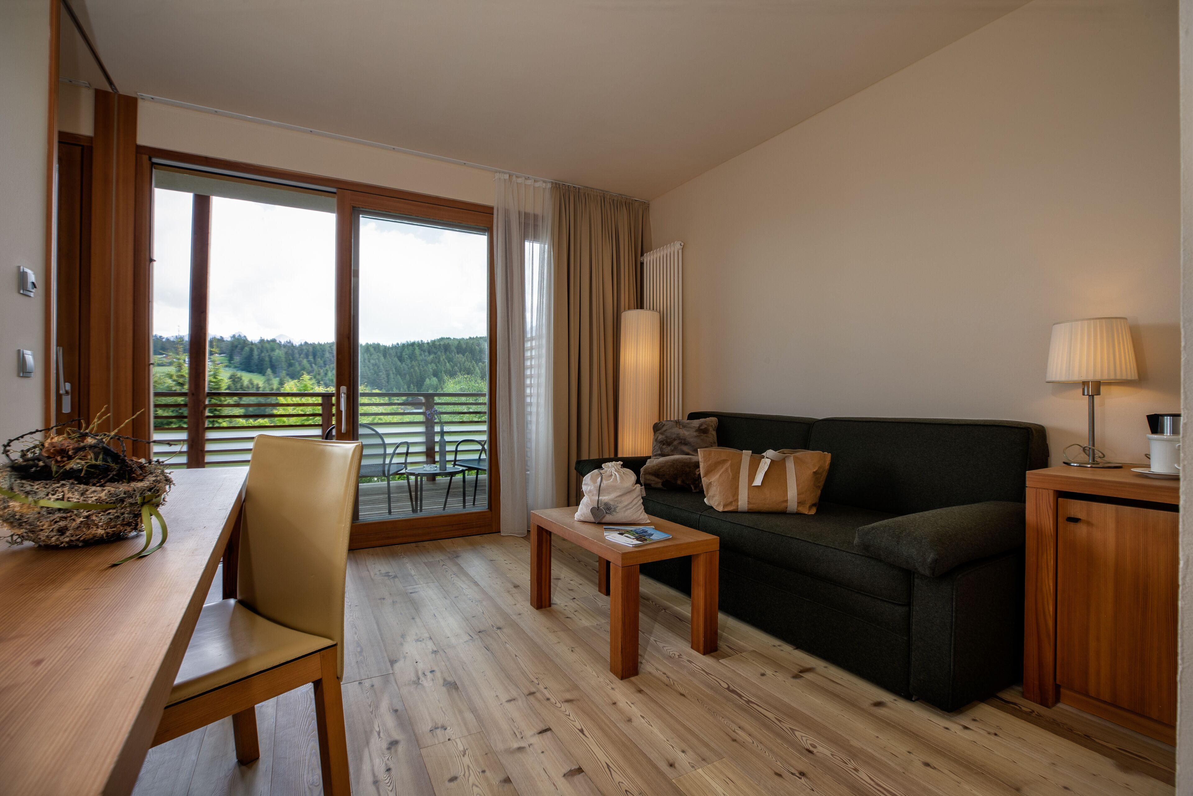 Uma sala de estar moderna com piso de madeira, um sofá verde, uma pequena mesa de madeira e uma área de jantar com mesa e cadeiras.
