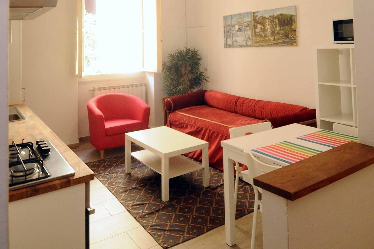 A compact living space with a kitchen, a red sofa, a white table, and a radiator.