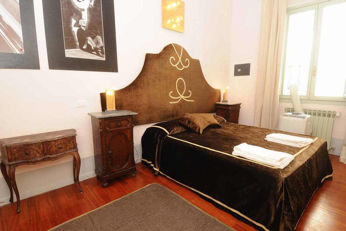 A bedroom with a large bed, a nightstand, a dresser, and a window with curtains.