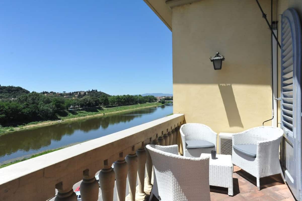 A balcony with wicker furniture overlooking a river and greenery.