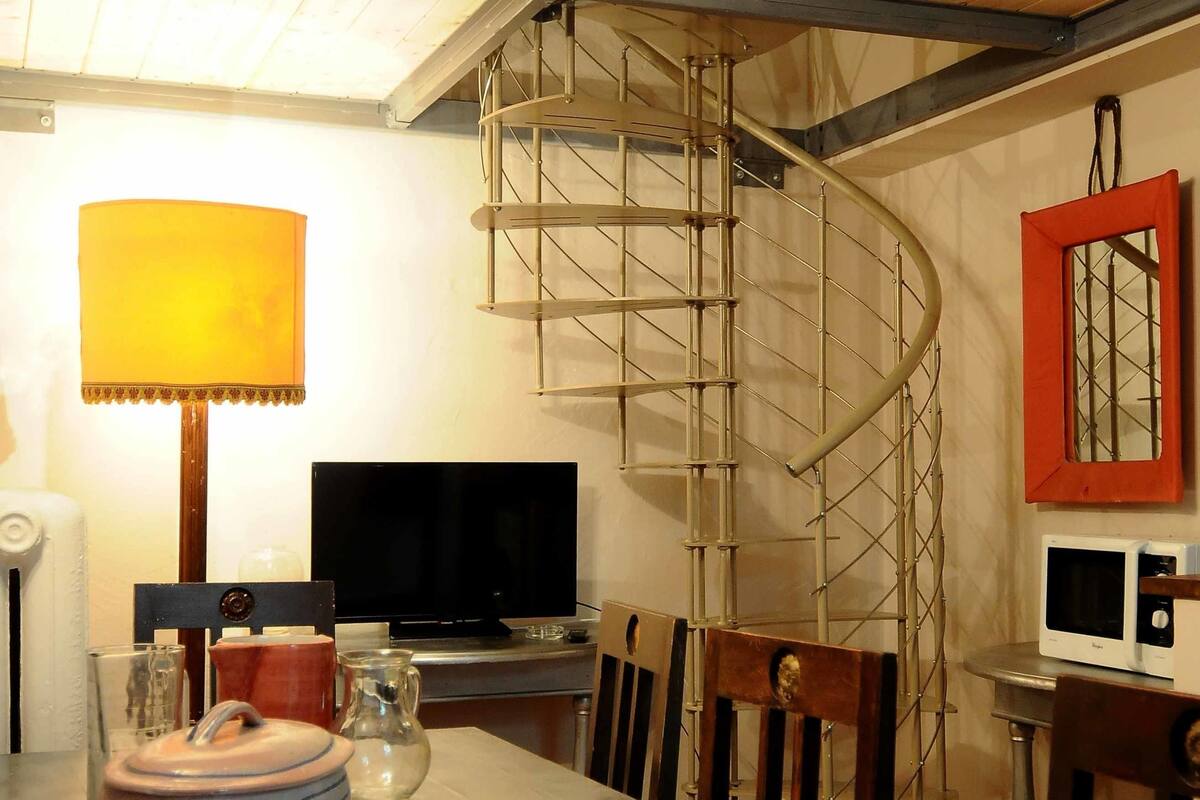 A dining area with a long table set for four, a television, and a spiral staircase.
