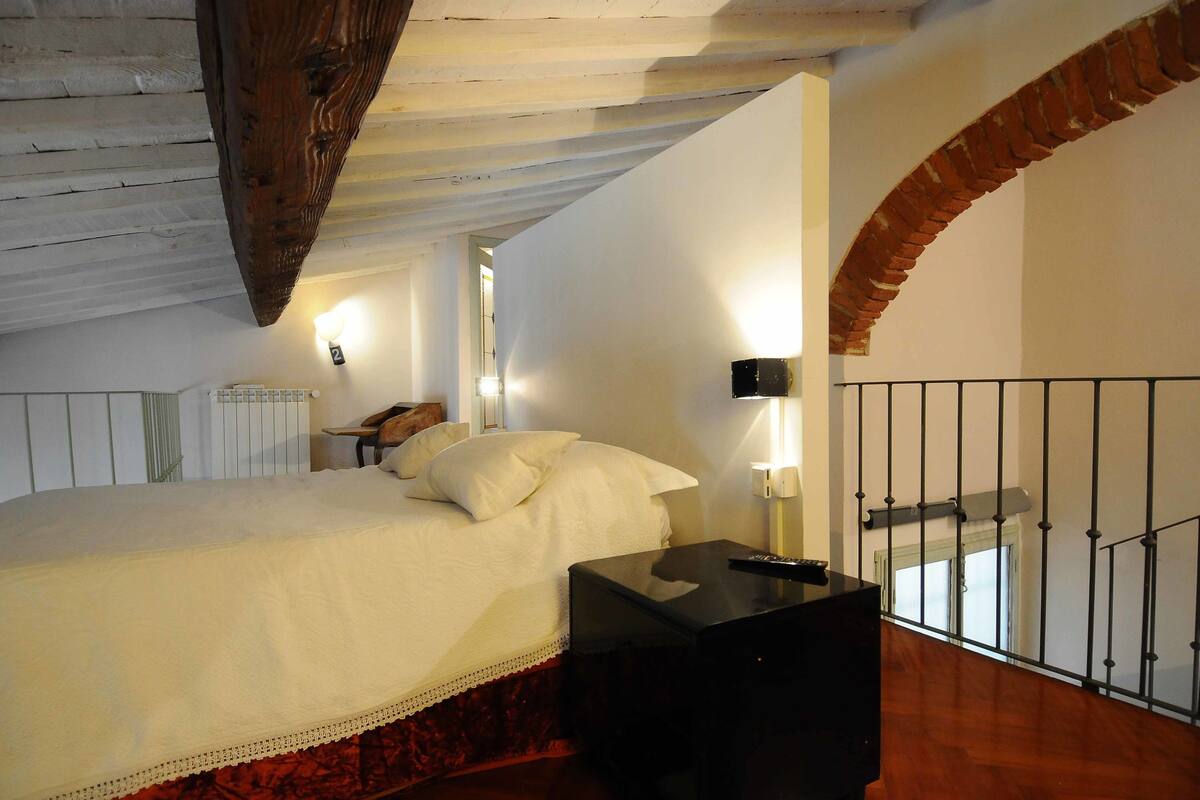 A bedroom with a bed, a nightstand, a lamp, and a view of a balcony.