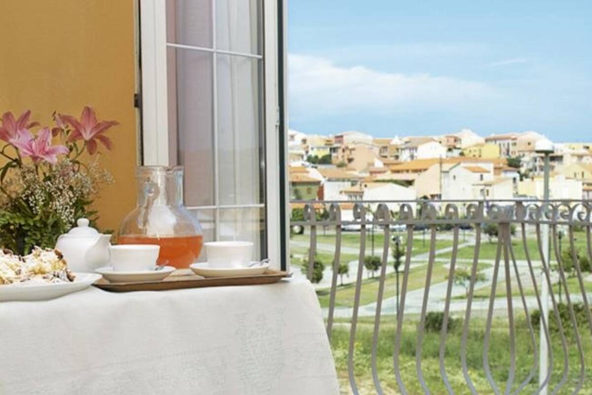 Ein Balkon mit Tisch, gedeckt für Tee, einer Blumenvase und Blick auf eine Wohngegend.