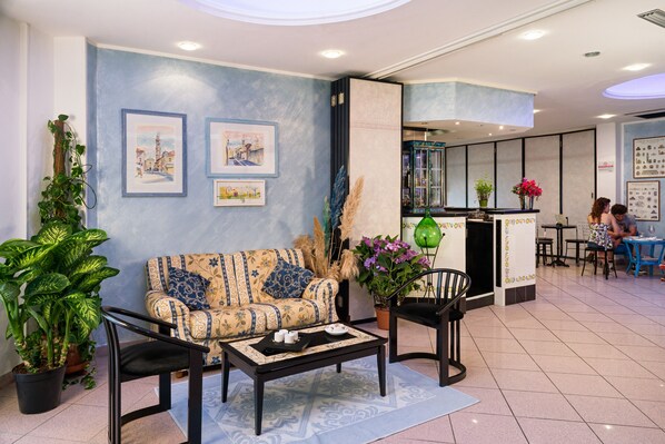 Un hall d’entrée moderne avec un canapé, une table basse et des fauteuils, un coin bar et des œuvres d’art encadrées accrochées aux murs.