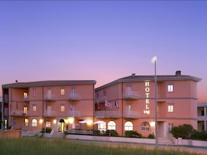 Un hôtel à la façade rose, doté de nombreux balcons et d’une entrée bien éclairée.