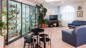 Een woonkamer met een glazen vitrine, een blauwe bank, een televisie en een potplant.