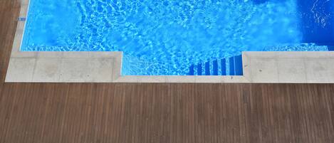 A swimming pool with clear blue water, surrounded by a wooden deck and lounge chairs with purple cushions.