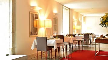 A dining area with tables set for a meal, chairs, and wall-mounted lamps.