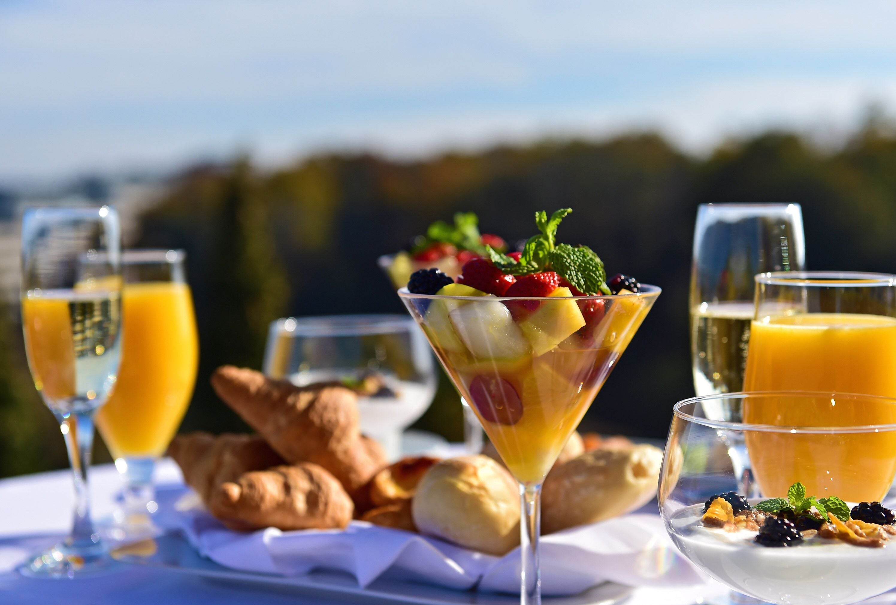 A table set with a fruit salad, croissants, and glasses of orange juice.